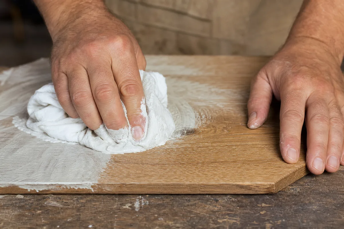 Chiffon de coton essuyant l’excédent de céruse sur un panneau de chêne brossé